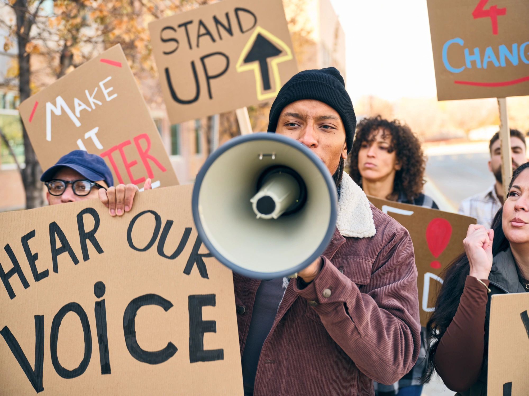Diverse group of people holding signs as a man speaks through a megaphone at a positive community rally